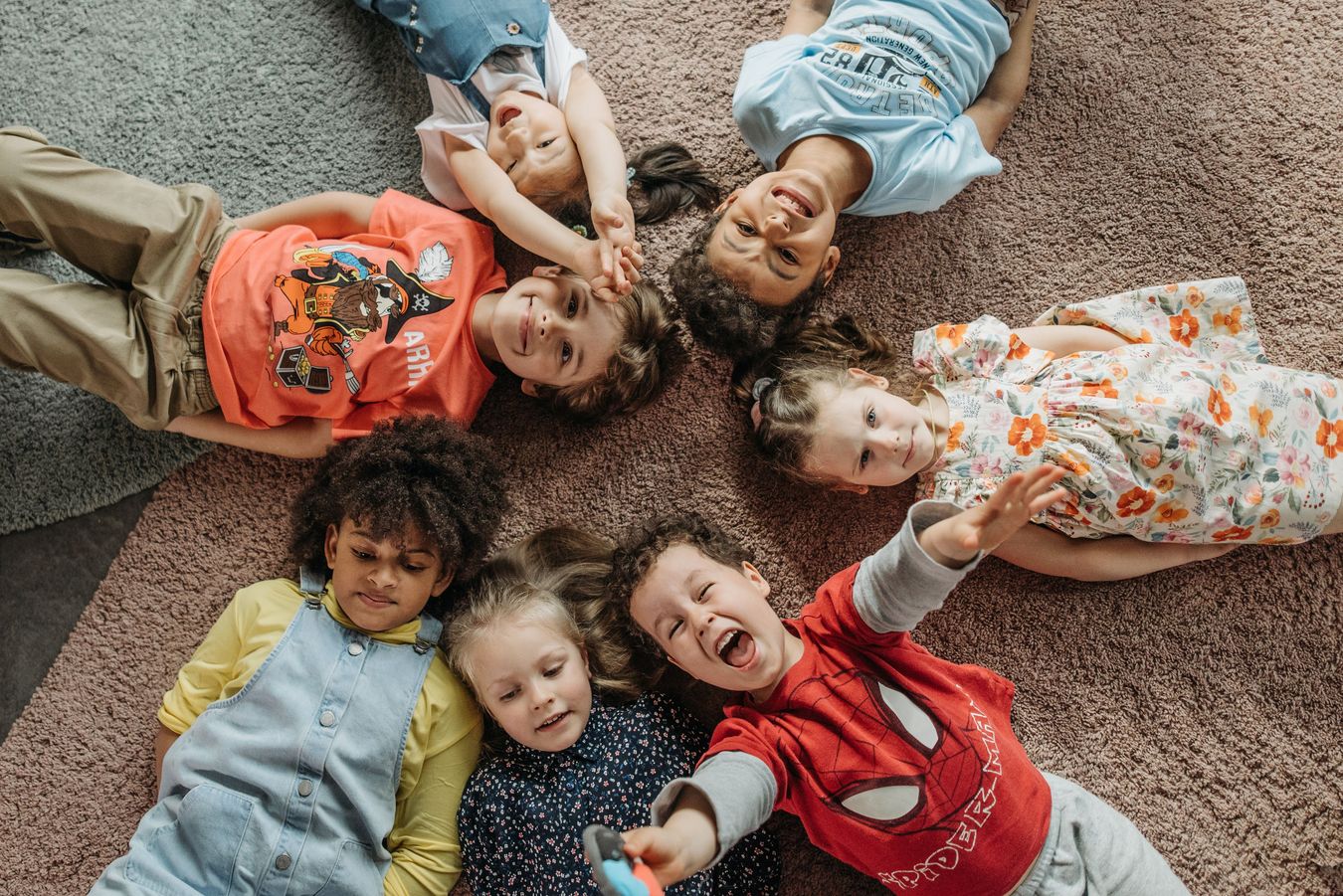 Kinder liegen im Kreis auf einem Teppich und lachen